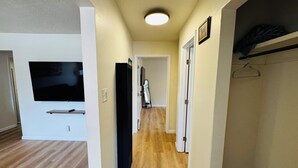 A hallway with a flat-screen TV mounted on the wall, wooden flooring, and a ceiling light. - Free Chick-fil-A & Starbucks! 502 Hideaway! (Farmington)