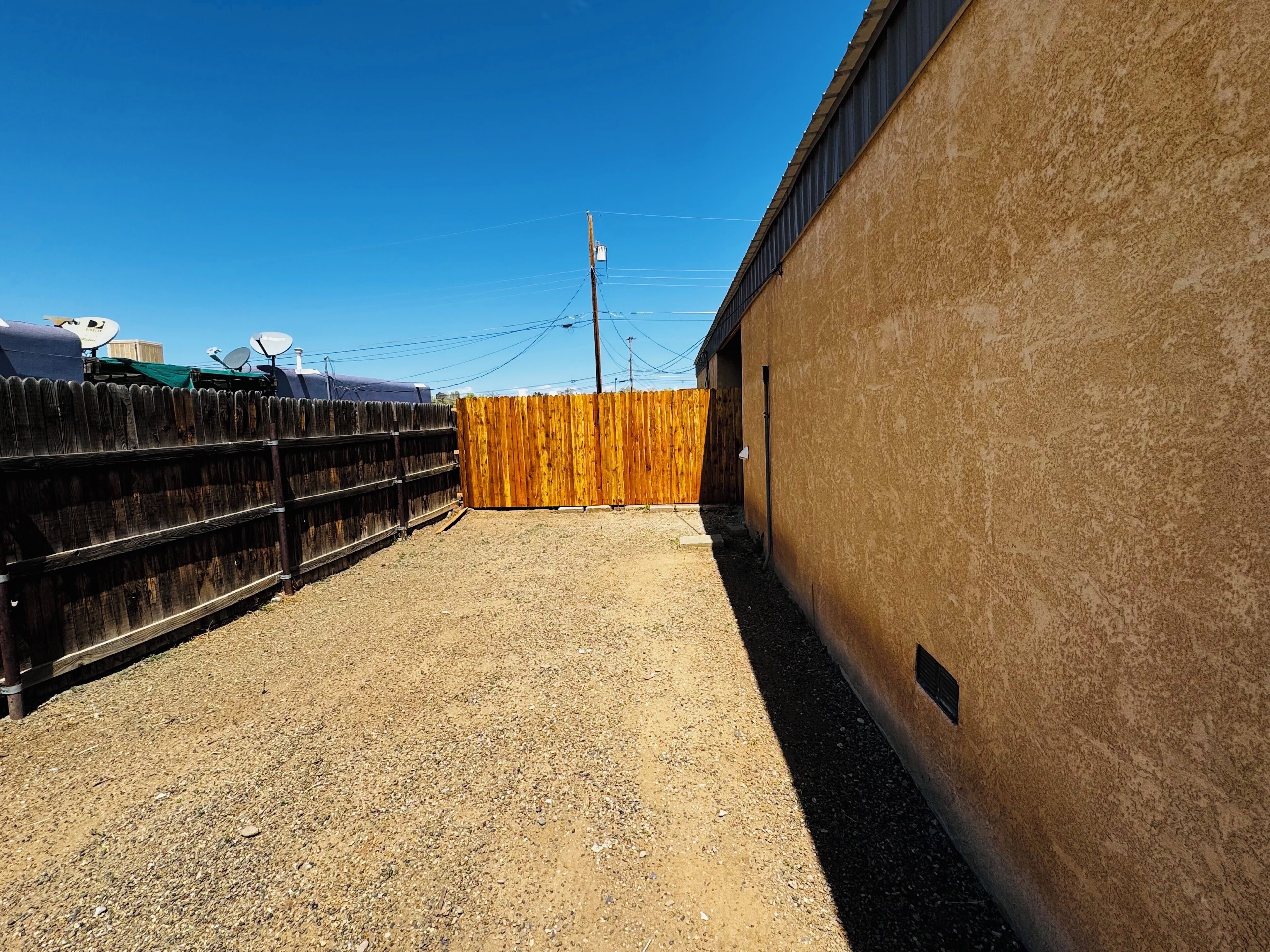 A fenced outdoor area with a gravel ground, a wooden fence, and a building with a textured wall.