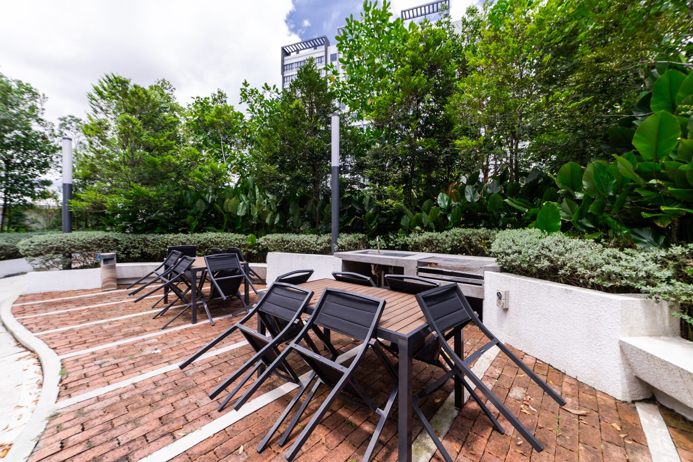 Une terrasse extérieure avec un sol en briques, des tables et des chaises en métal.