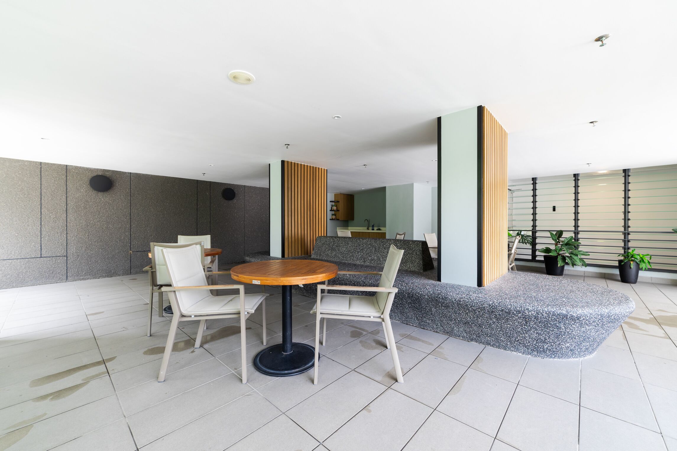 A modern indoor space with a round table and chairs, a grey bench, and potted plants.