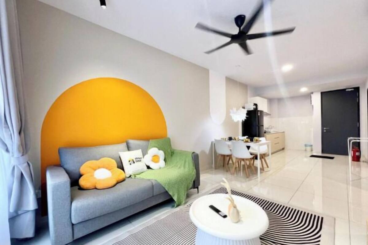 Een moderne woonkamer met een grijze bank, een ronde gele accentmuur en een plafondventilator.