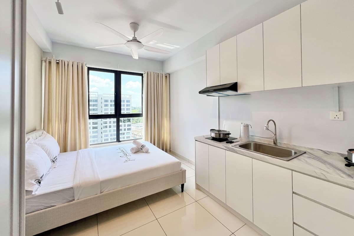 Een moderne hotelkamer met een bed, een raam met gordijnen, een plafondventilator en een kitchenette met een spoelbak en aanrecht.