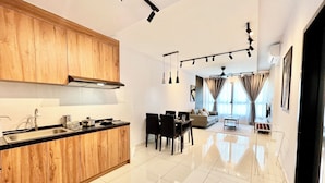 A modern kitchen with wooden cabinets, a dining area with a table and chairs, a living room with a sofa, and a ceiling fan. - Gaia Residences by Sleepy Bear (Rawang)