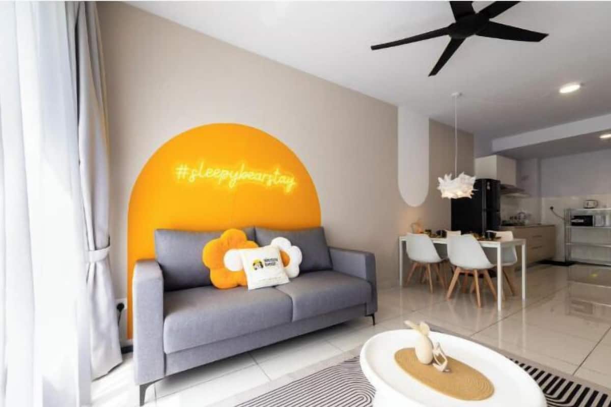 Een moderne woonkamer met een grijze bank, een neonbord en een eethoek met witte stoelen.