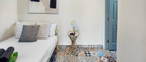 A bedroom with a bed, a small side table with a lamp, a wall-mounted air conditioner, and a patterned floor.
