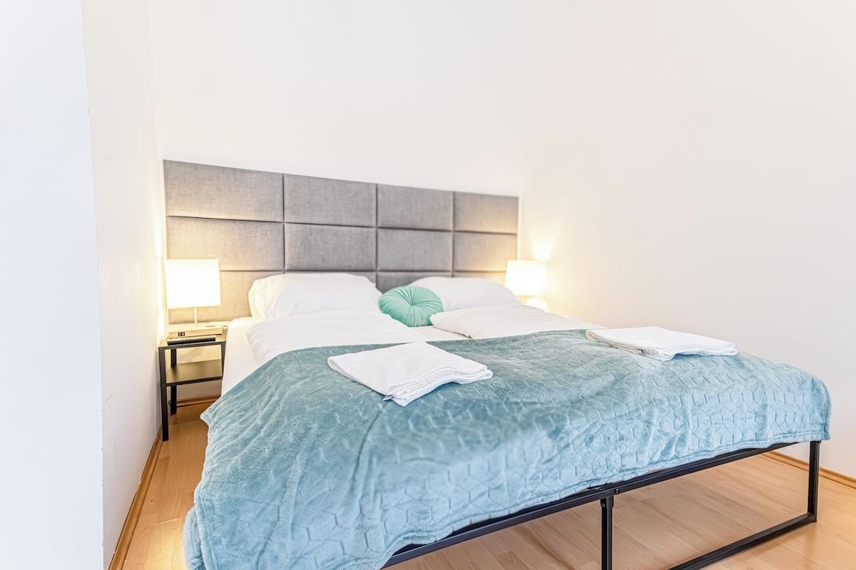 A neatly made bed with a blue quilt, two bedside lamps, and a grey headboard.