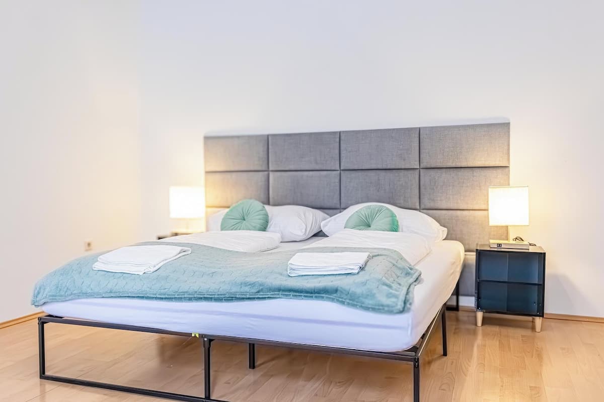 A neatly made bed with a grey headboard, two bedside lamps, and a small bedside table with a lamp.