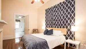 Une chambre avec un plancher en bois, un lit recouvert d’une couette grise et blanche, deux lampes de chevet et une tête de lit à motifs.