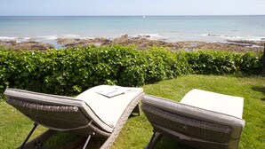 Two wicker lounge chairs with cushions facing a rocky beach and ocean view.