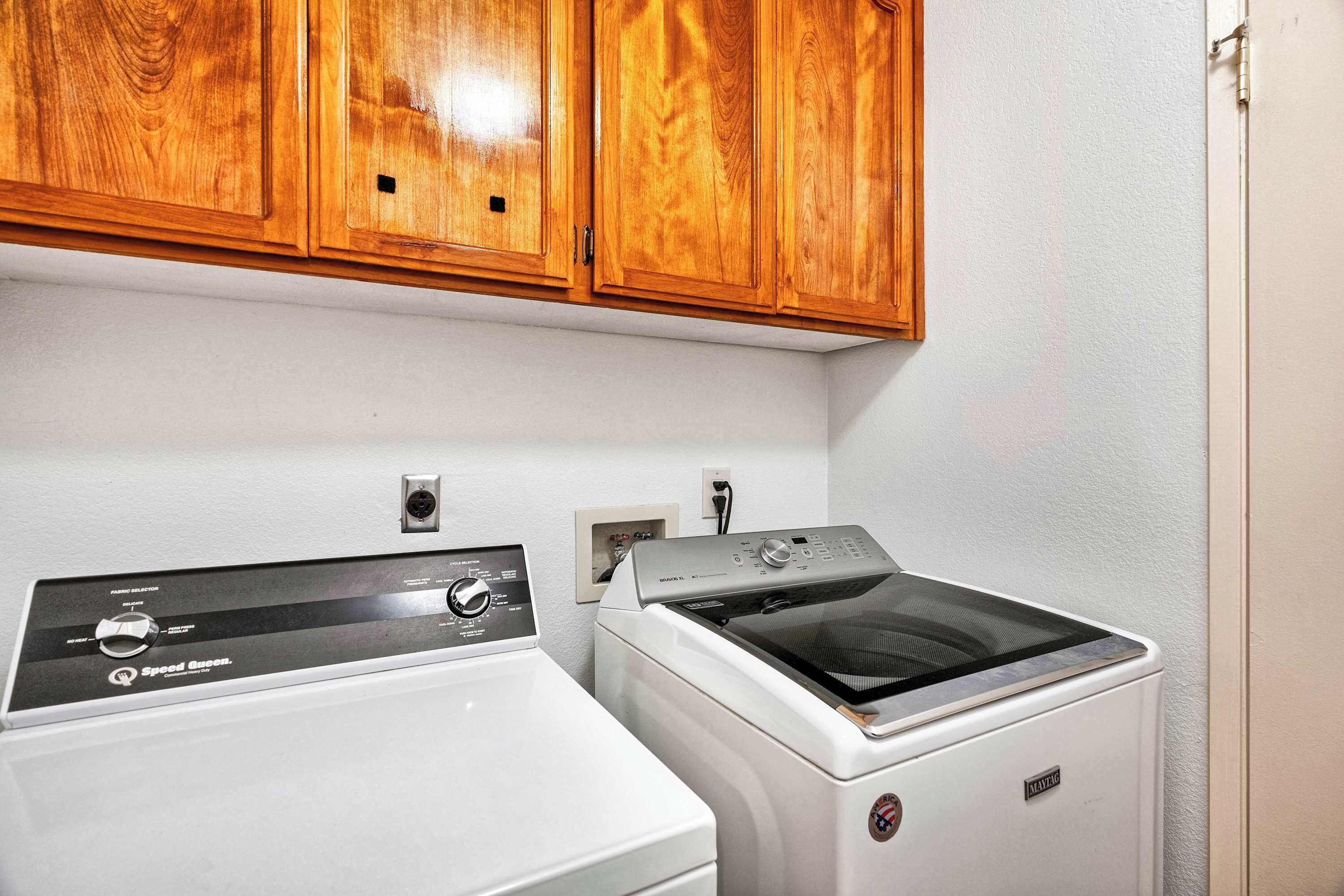 A laundry area with two washing machines and wooden cabinets above.