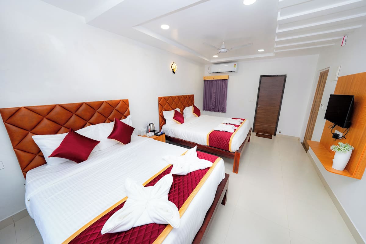A hotel room with two beds, each with a wooden headboard, white bedding, and red accents. There is a wooden shelf with a plant, a wall-mounted TV, and an air conditioning unit.
