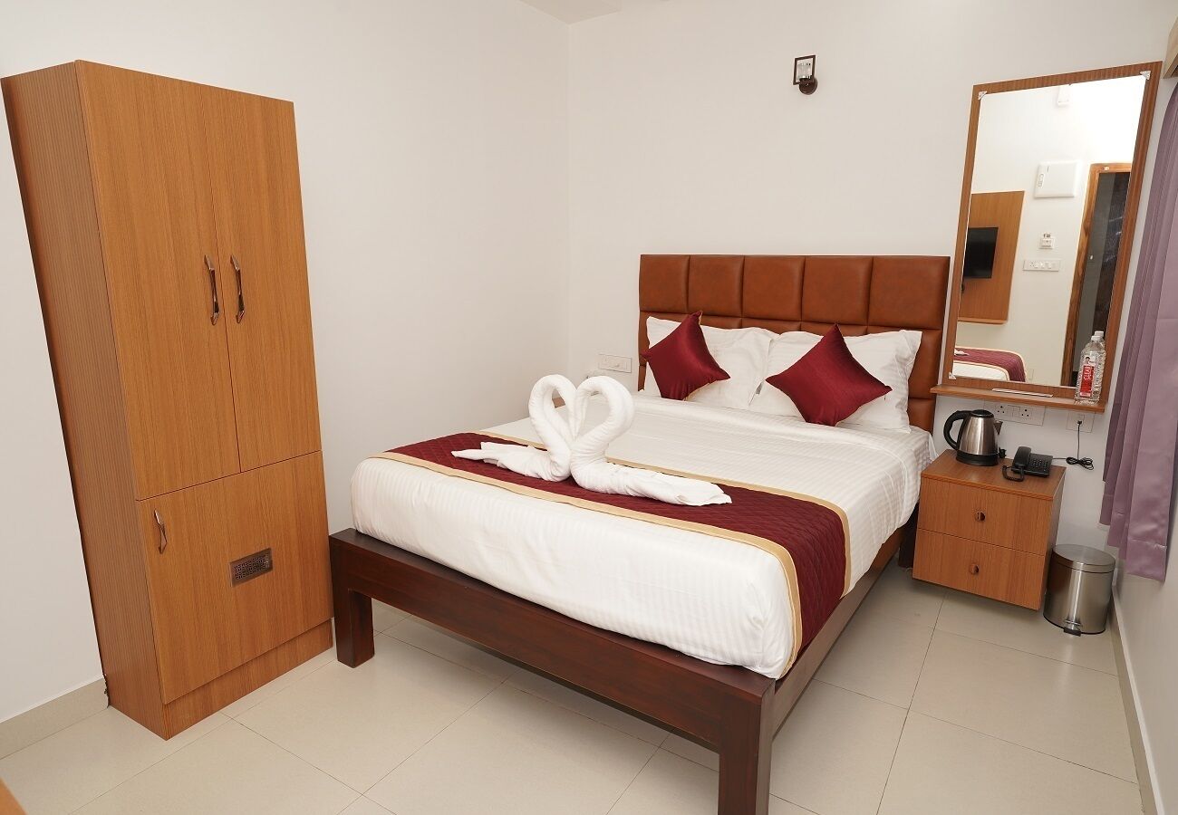 Una cama bien hecha con una colcha roja y blanca, un armario de madera y una mesita de noche con una tetera y un teléfono.