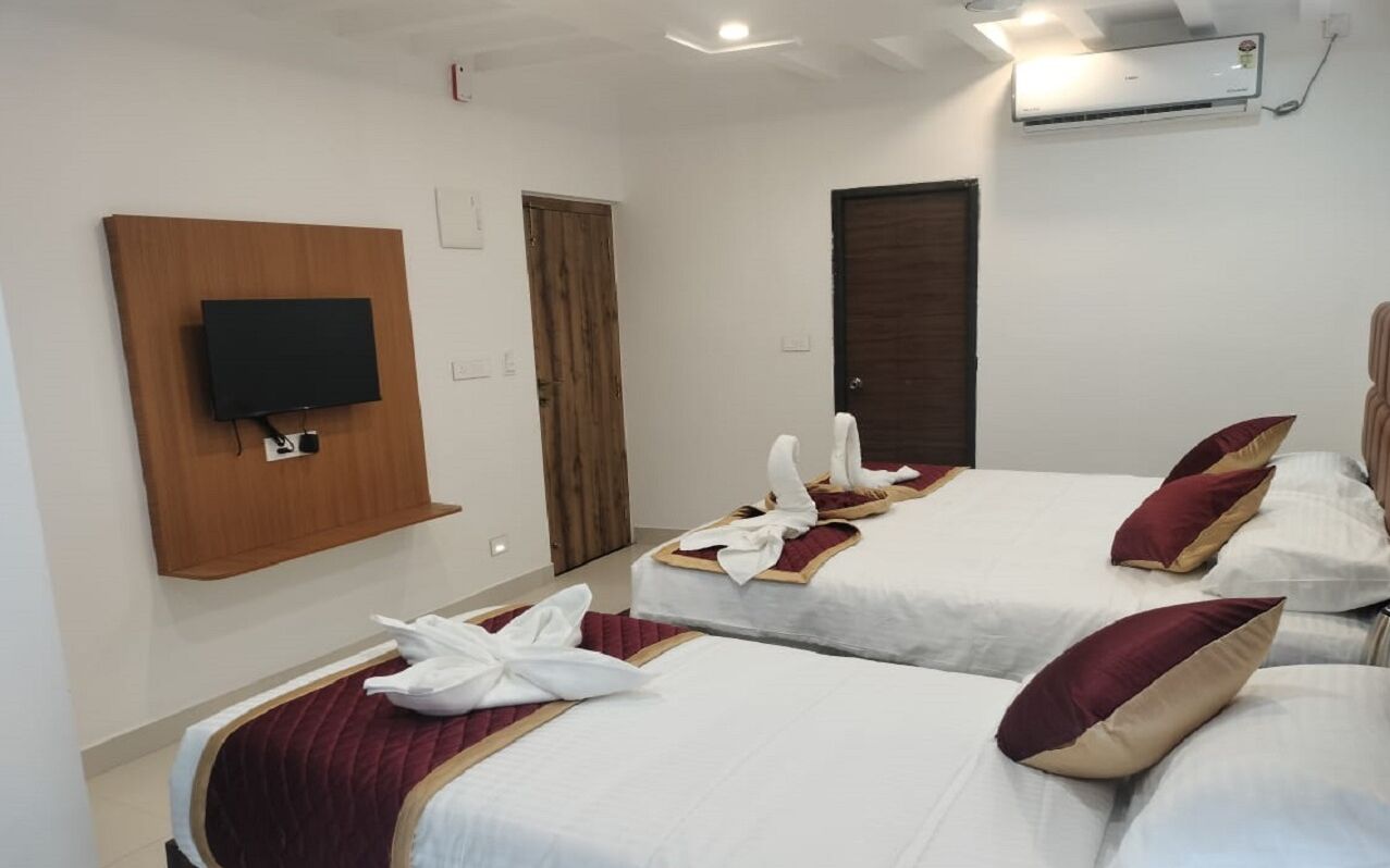A hotel room with two beds, a flat-screen TV mounted on a wooden panel, an air conditioning unit, and a wooden door.
