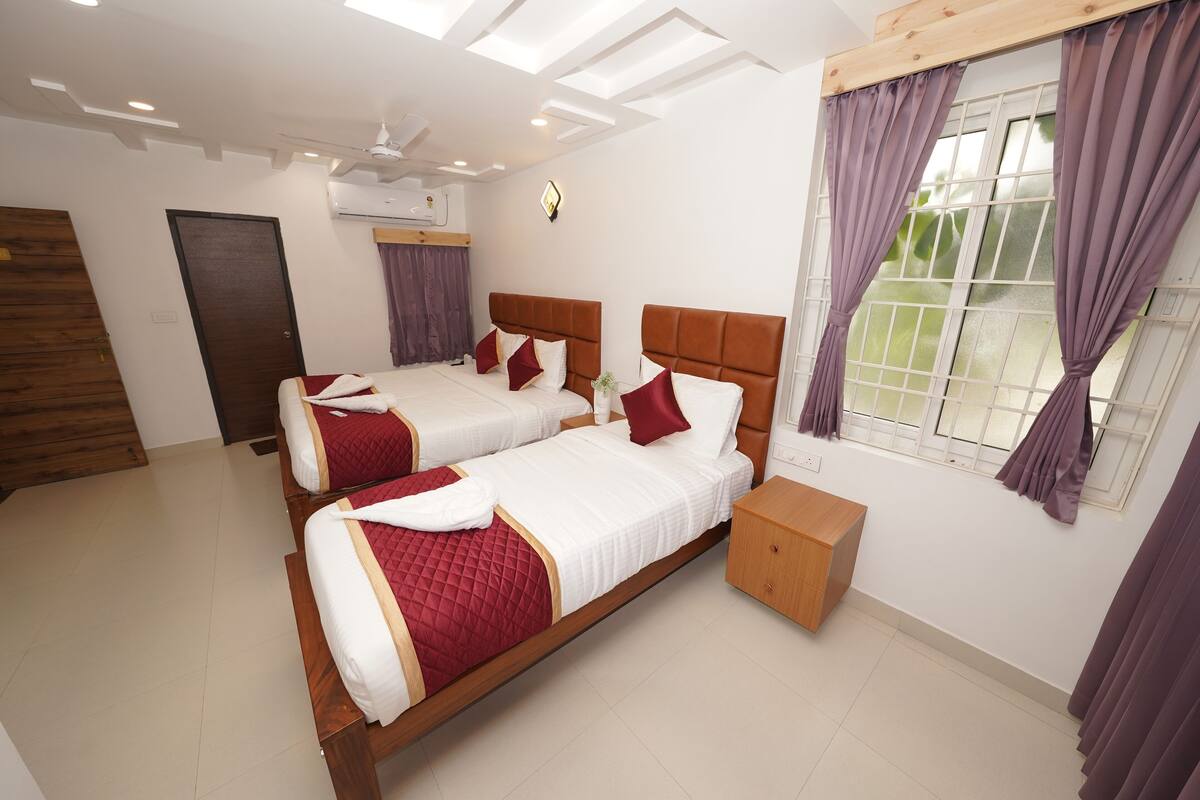 A hotel room with two beds, a wooden nightstand, a window with purple curtains, and a ceiling fan.