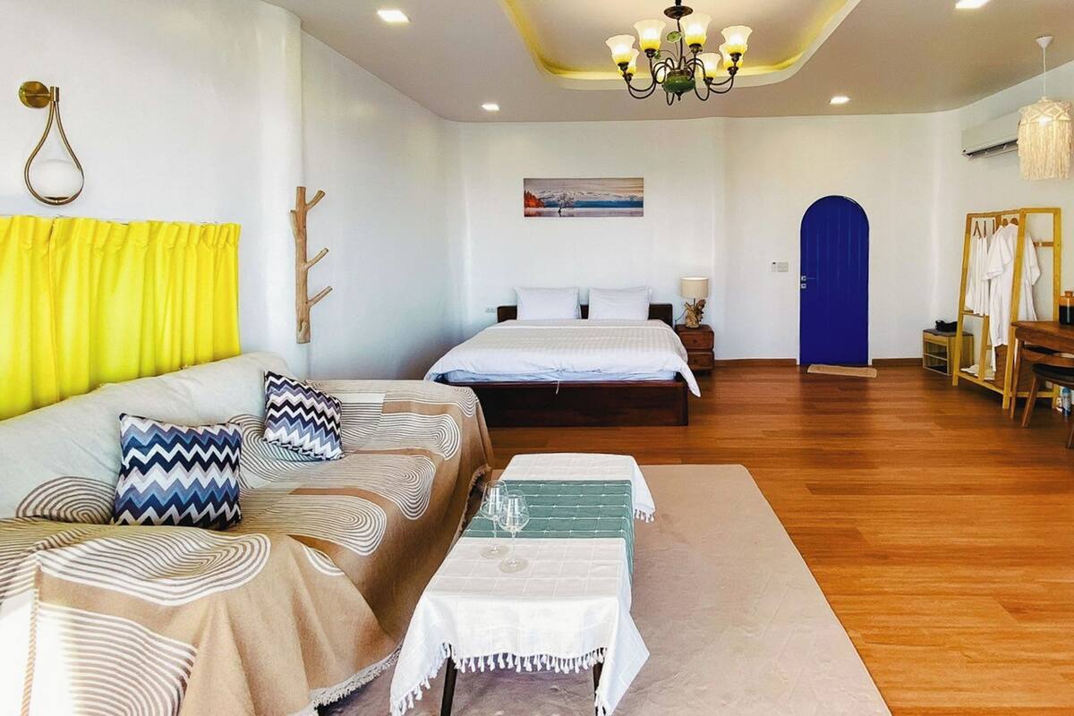 A modern hotel room with a bed, a sofa, a dining table, and a mirror.