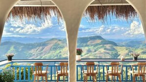 A balcony with a view of mountains, wooden chairs, and hanging lights. - Nontawa Villa Doichang (Mae Suai)