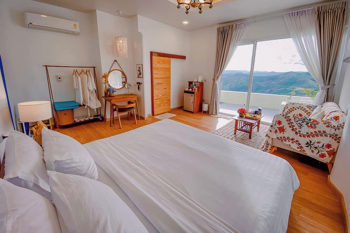 A hotel room with a large bed, a desk with a chair, a vanity with a mirror, and a view of the mountains through the window.