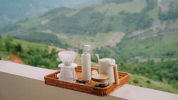 Una bandeja de mimbre con equipo para preparar café en un balcón con vistas a un paisaje montañoso.