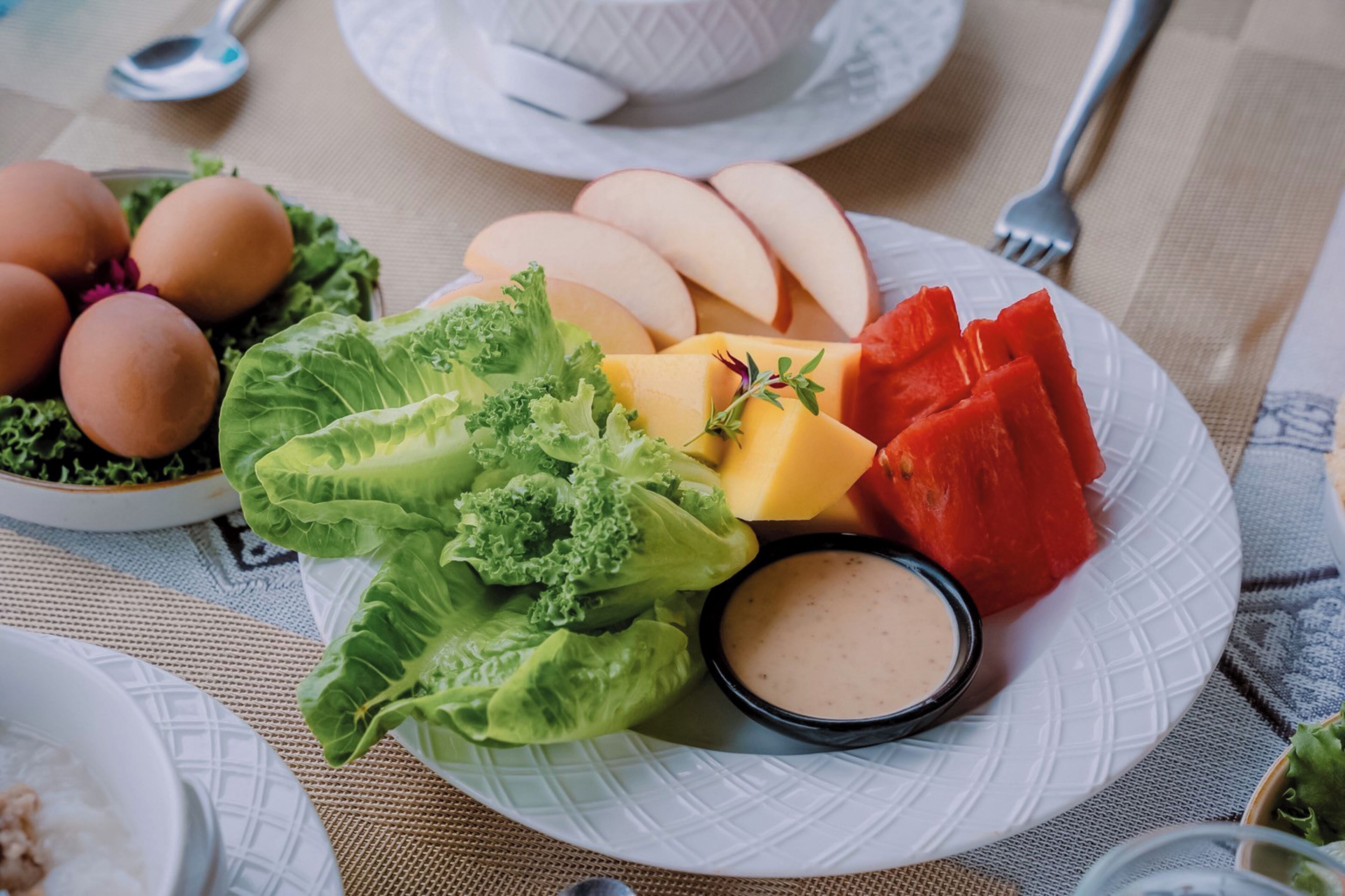 A plate with eggs, lettuce, apples, watermelon, and a dipping sauce.