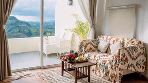 A living room with a sofa, a coffee table, and a view of a balcony with a plant and a chair. - Nontawa Villa Doichang (Mae Suai)