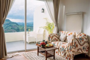 Un salon avec un canapé, une table basse et une vue sur un balcon agrémenté d’une plante et d’une chaise.