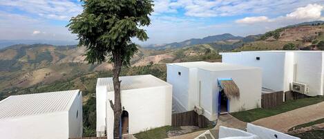 A rural village with white buildings, a tree in the foreground, and a hilly landscape in the background.