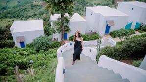 A person walking on a staircase surrounded by white buildings with blue doors, set against a lush green landscape. - Nontawa Villa Doichang (Mae Suai)