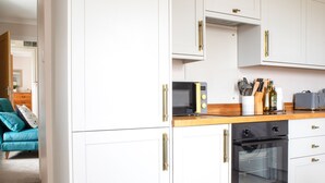 A modern kitchen with white cabinetry, a wooden countertop, a microwave, a toaster, and a stove. - Taigh Mhurdaidh by Interhome (North Skye)
