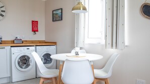 A compact kitchen with a washing machine, a dining table with chairs, a pendant light, and a fire safety poster. - Taigh Mhurdaidh by Interhome (North Skye)