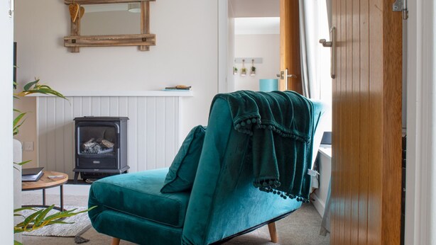 A teal armchair with a blanket, a wood-burning stove, and a mirror on the wall. - Taigh Mhurdaidh by Interhome (North Skye)