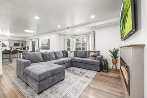 A modern living room with a grey sectional sofa, a small ottoman, and a fireplace.