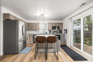 Una cocina moderna con electrodomésticos de acero inoxidable, piso de madera y un amplio ventanal corredera que da a un patio trasero.