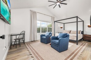 Un dormitorio con una cama con dosel, dos sillones, un escritorio y un ventanal grande.