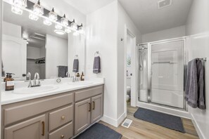A modern bathroom with a double sink vanity, a large mirror, and a glass shower enclosure.