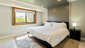 Une chambre moderne avec un grand lit, une table de chevet, une fenêtre offrant une belle vue et des spots encastrés au plafond.