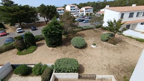 A residential area with multiple apartment buildings, a parking lot with several cars, and various landscaped areas including bushes and trees.