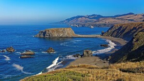 A coastal landscape with rocky cliffs, a sandy beach, and a clear blue sea. - Cabana Del Rio, by Vinifera Homes (Guerneville)
