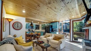 A cozy living room with a fireplace, a dining area, and a kitchen with blue cabinets. - Cabana Del Rio, by Vinifera Homes (Guerneville)