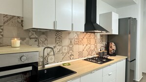 Une cuisine moderne avec des armoires blanches, une hotte noire, une cuisinière à gaz, un réfrigérateur en acier inoxydable et des carreaux décoratifs sur le mur derrière l’évier.