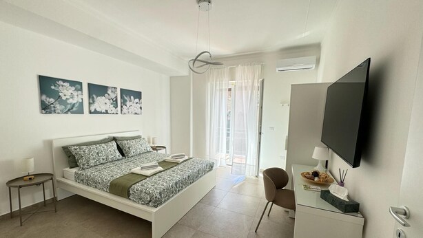 Une chambre à coucher moderne, avec un lit, des tables de chevet, un bureau, une chaise, un téléviseur à écran plat et des œuvres d’art accrochées au mur.