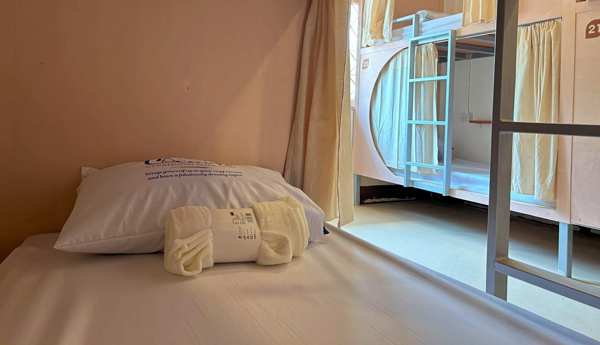 A hotel room with a bunk bed, a pillow with text, and a window with curtains.