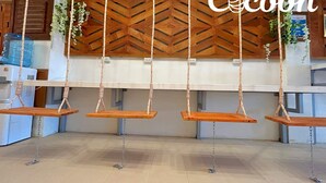 Habitació amb quatre seients de fusta penjants del sostre, una paret de fusta amb dibuixos en zig-zag i un paviment de rajoles.
