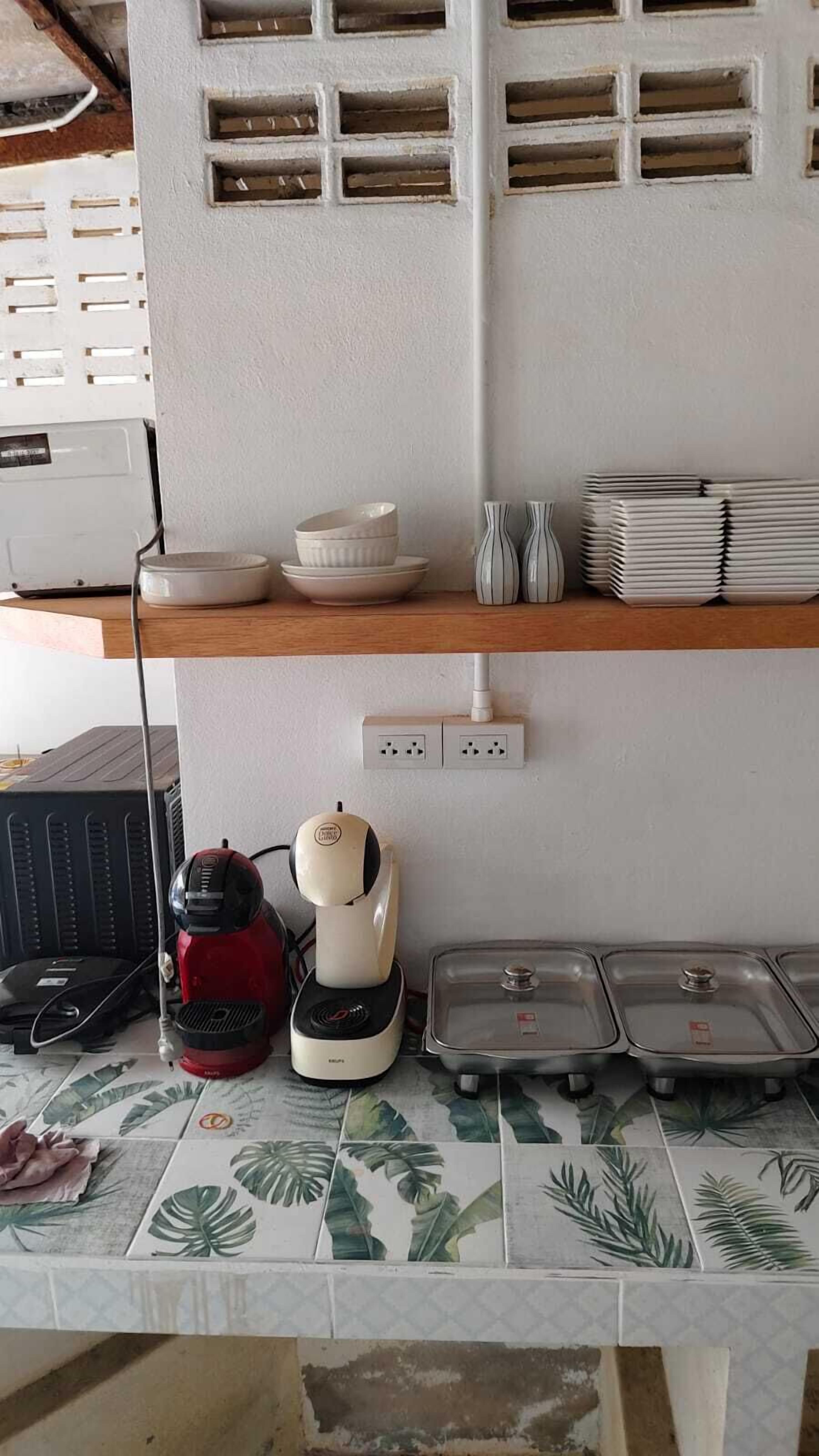 Una cocina con una encimera, un hervidor, una olla arrocera y una pila de platos.