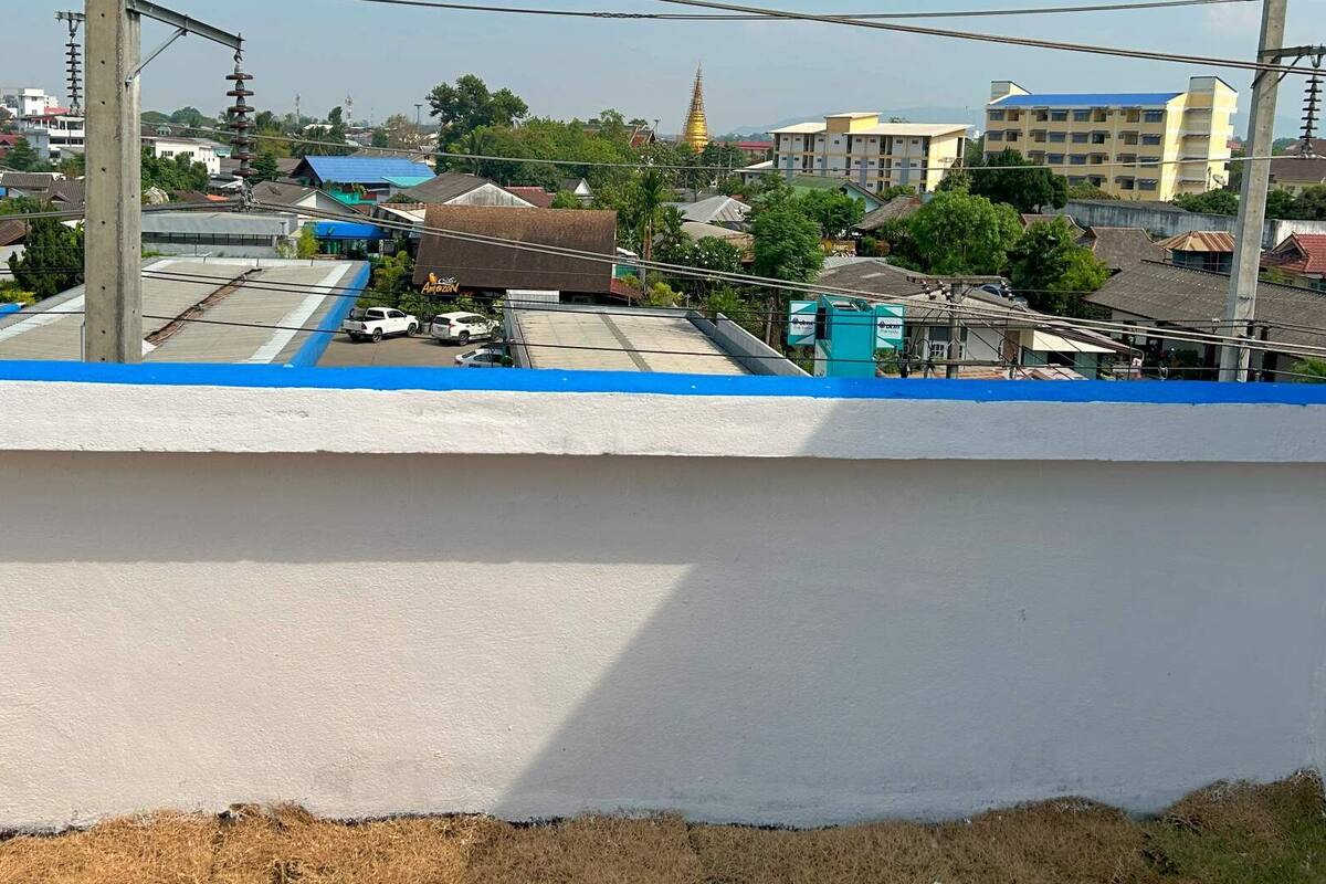 Une vue d’un bâtiment doté d’un toit plat, entouré d’autres constructions et de végétation.