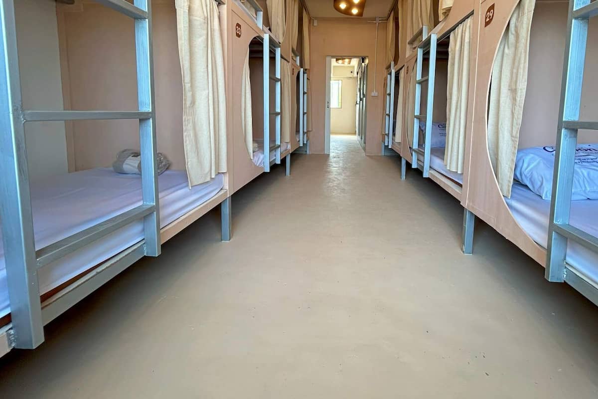 Un couloir avec des lits superposés, chacun étant équipé d’un rideau et d’un oreiller.
