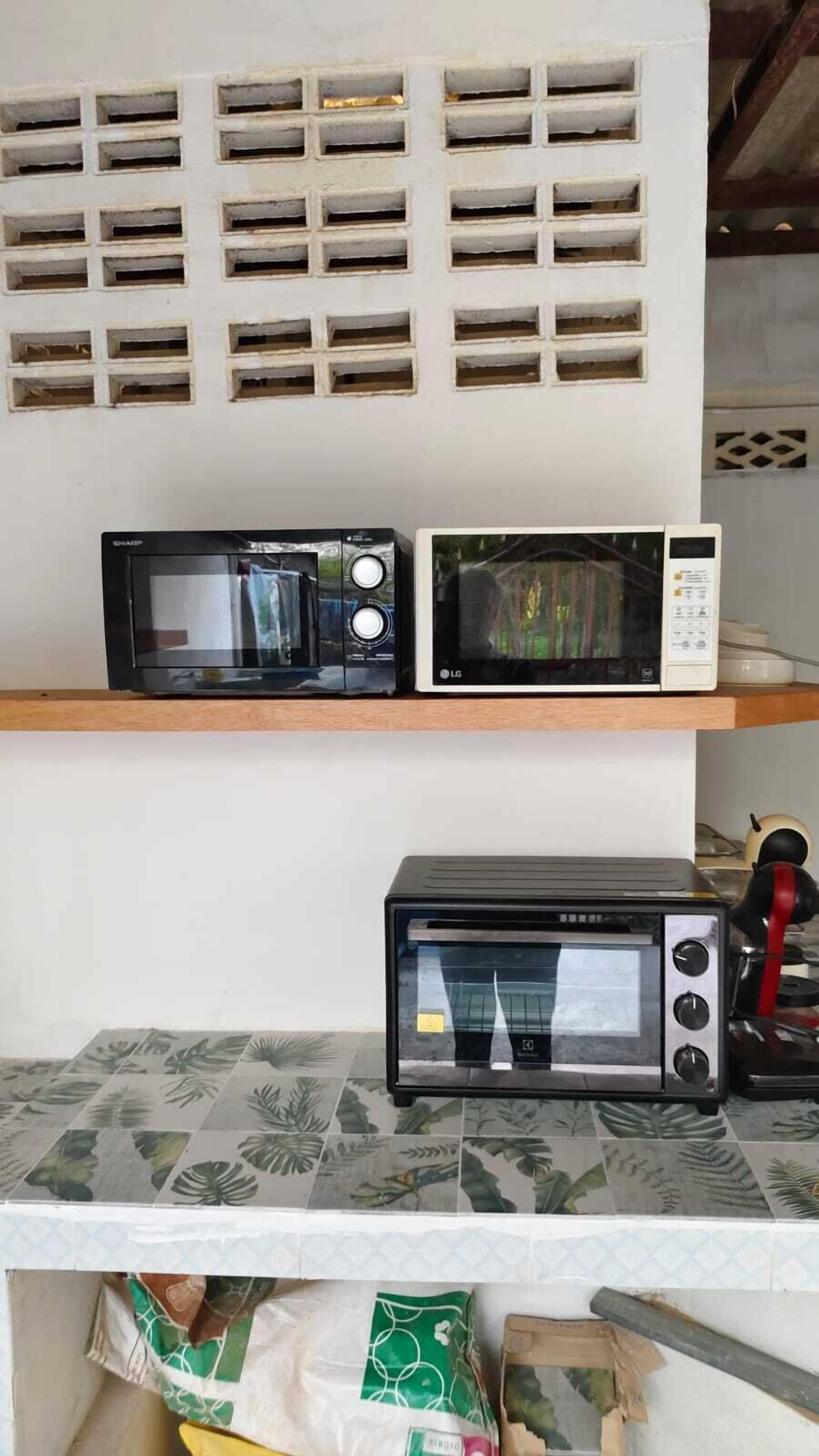 A kitchen with two microwaves on a shelf, a toaster oven on the counter, and a wall with ventilation holes.