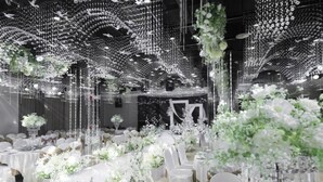 An indoor venue with tables set for a formal event, adorned with white floral arrangements and a ceiling decorated with hanging lights and floral designs. - Wanzai Yijia La Maison Hotel (Yichun)