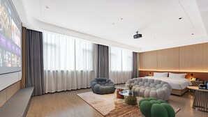 A modern hotel room with a large bed, a seating area with two bean bags, a small coffee table, and a large window with curtains. - Wanzai Yijia La Maison Hotel (Yichun)