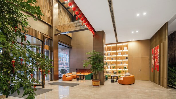 A modern lobby with a large seating area, a potted plant, and a wall with shelves displaying various items. - Wanzai Yijia La Maison Hotel (Yichun)