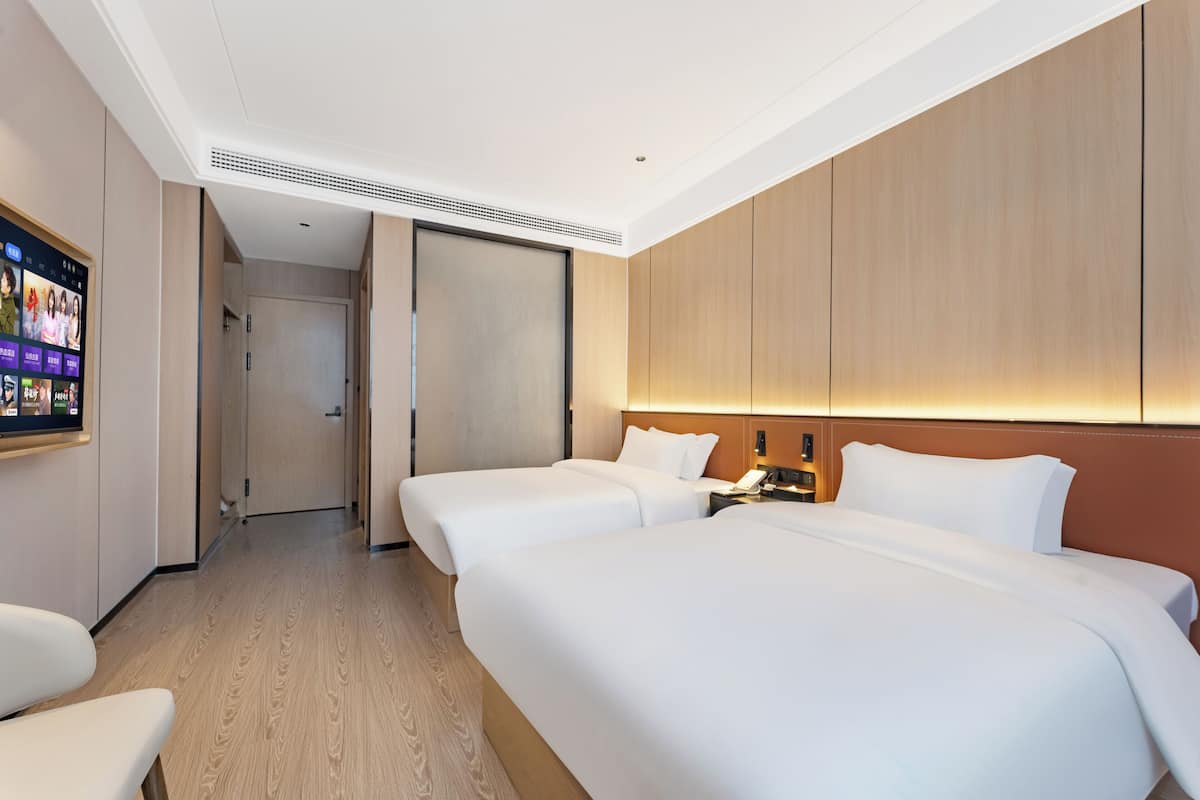 Quarto de hotel com duas camas, televisão fixada na parede e painel de madeira na parede.